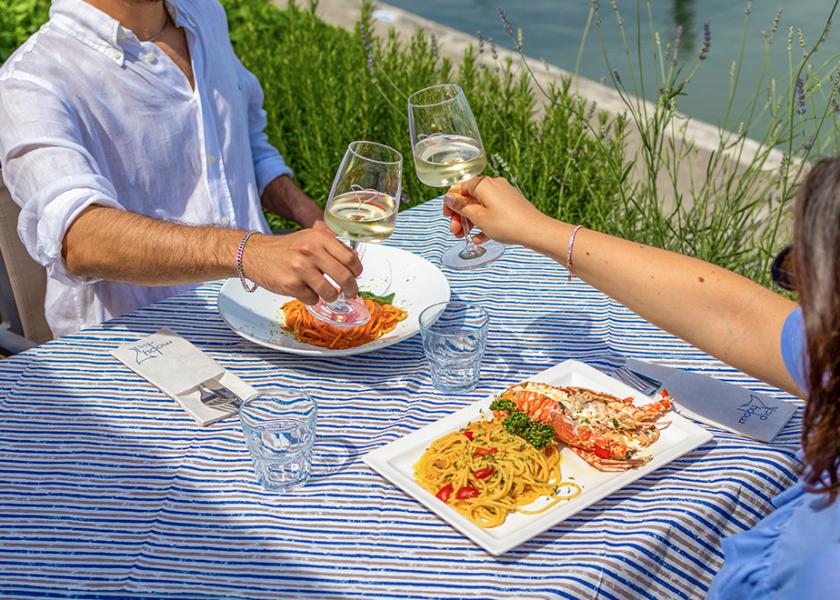 Due persone brindano con vino bianco su una tavola estiva all'aperto.