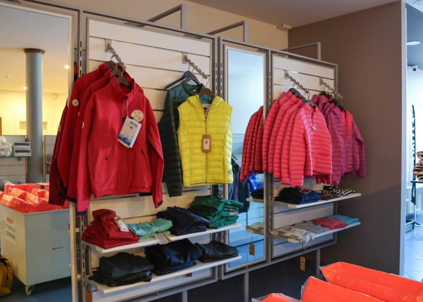 Giubbotti colorati appesi in un negozio di abbigliamento, con scaffali di maglie piegate.